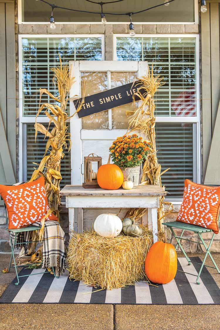 fall vignette on front porch with orange throw pillows, pumpkin and repurposed vintage window as word art