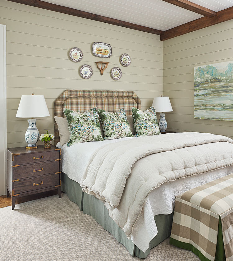 Antique-inspired plates hang of the bed frame, whose headboard is a rich plaid fabric made in the same colors as the bench at the foot of the bed.
