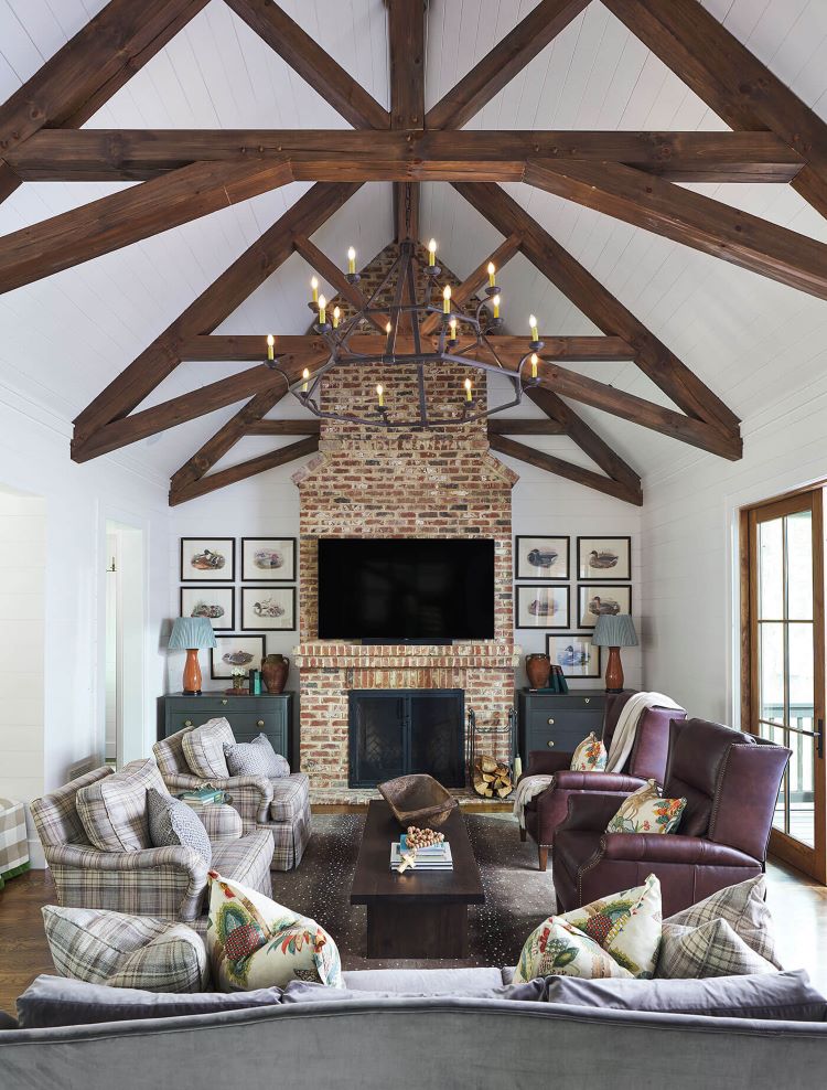 Dark wood beams chris cross across a white ceiling, drawing eyes upward, while matching waterfowl images and pottery-inspired lamps play up the symmetry of the both sides of a brick fireplace.