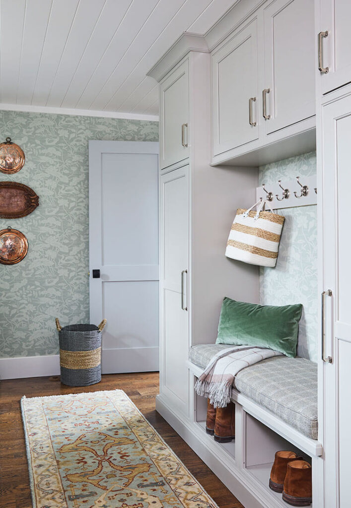The combined laundry room and mudroom leans darker with the darker green wallpaper. White cabinetry offsets the color while hanging plates made from wood and copper render pops of rich hues.