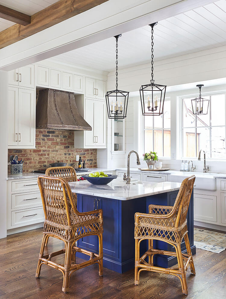 Brick backsplash offers texture against an almost all white kitchen except for a wood floor and a brilliant blue island.