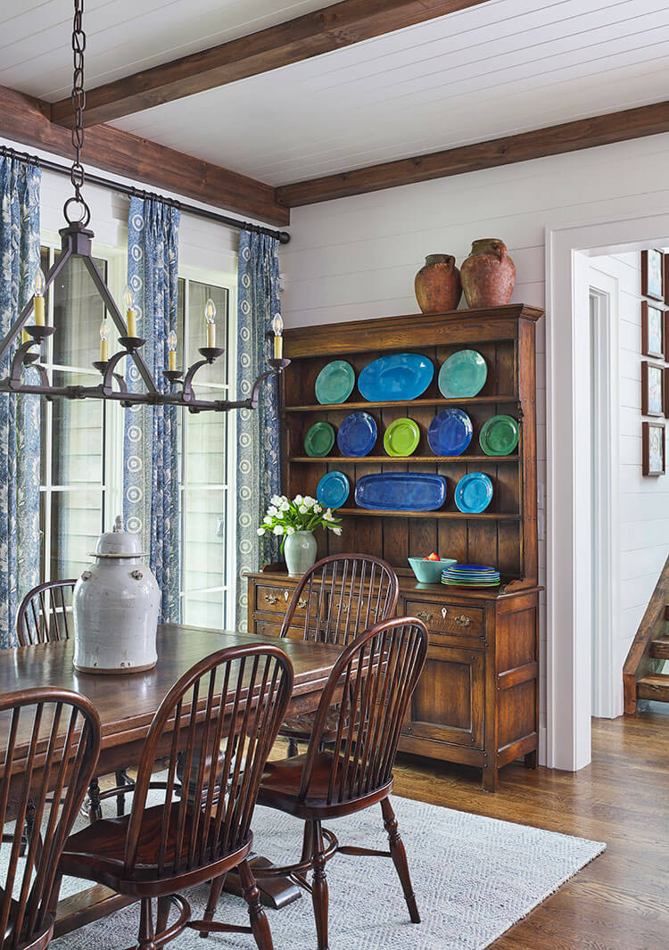 Blue and green pottery plates in various shades line the dark wood hutch that sits on the wall facing the farmhouse dining table