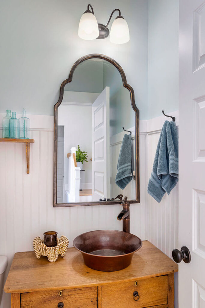 Powder bathroom with wainscoting and green glass on an open shelf