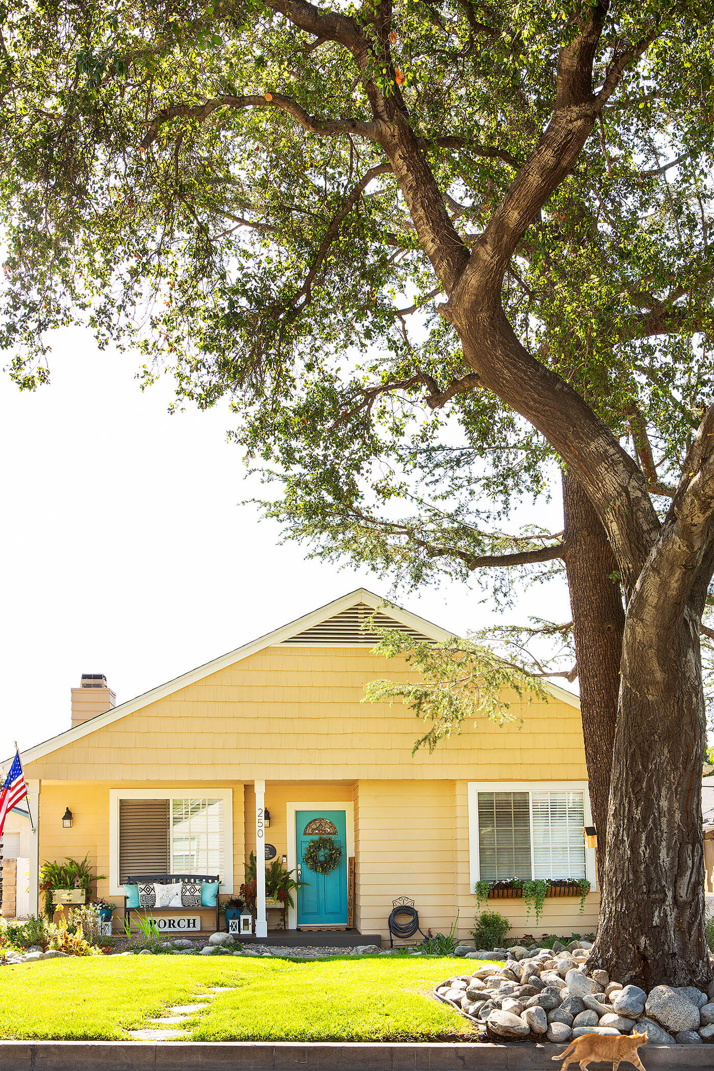 Exterior of yellow farmhouse with cute front porch and blue door