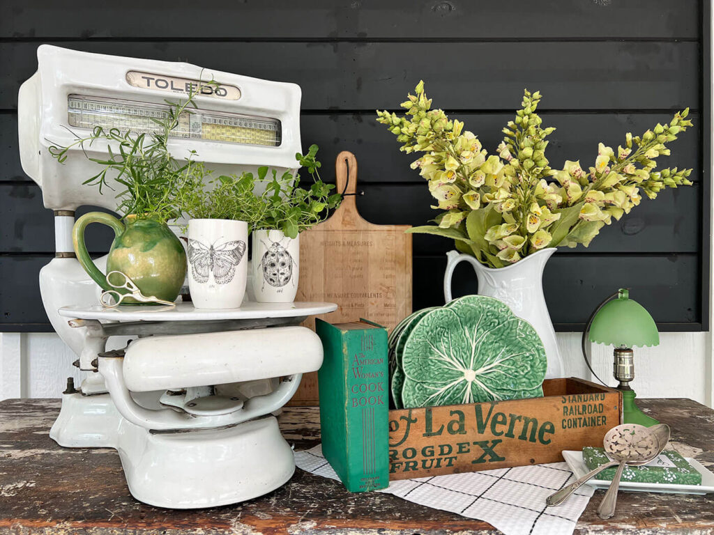 Decorating vignette with green vintage items and antique scale with herb garden