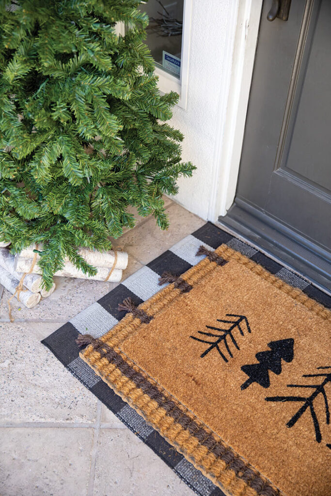 layered welcome mats and faux Christmas tree on front porch