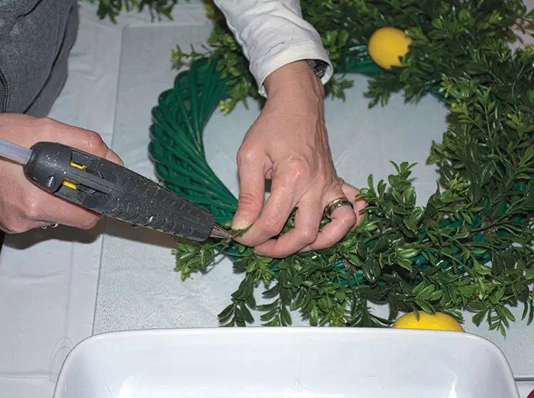 glueing faux greenery for wreath