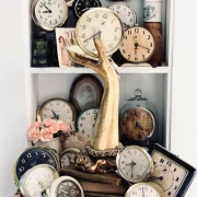 collection of vintage clocks arranged on a bookshelf with brass hand and other antiques