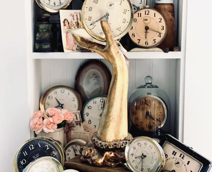 collection of vintage clocks arranged on a bookshelf with brass hand and other antiques