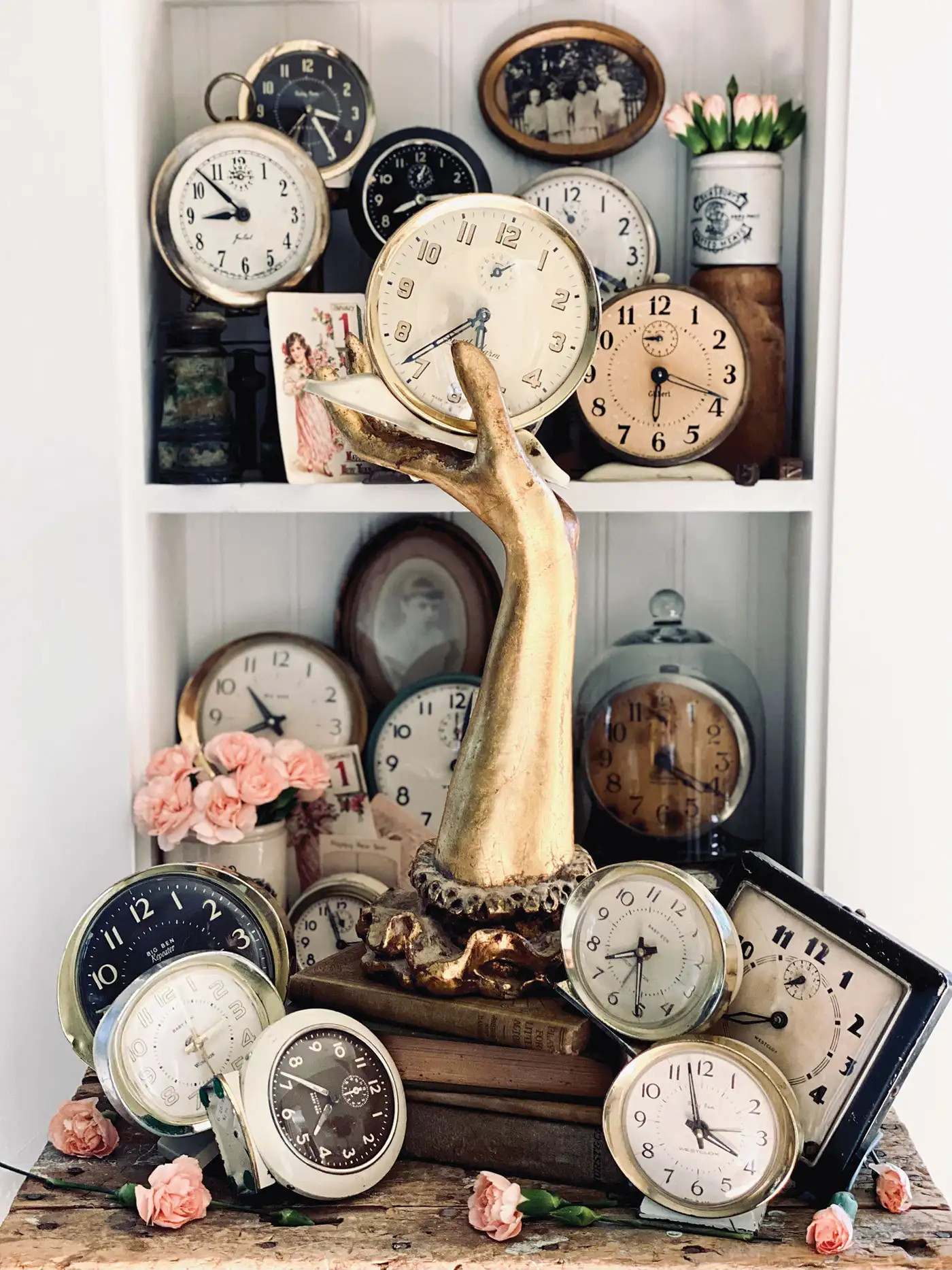 collection of vintage clocks arranged on a bookshelf with brass hand and other antiques