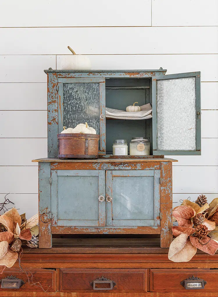 blue and rusted small hutch containing decorative white pumpkins and candles