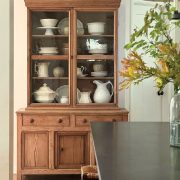 wooden hutch with white serveware and vase of fall leaves in dining room