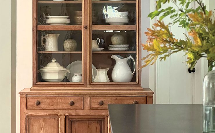 wooden hutch with white serveware and vase of fall leaves in dining room