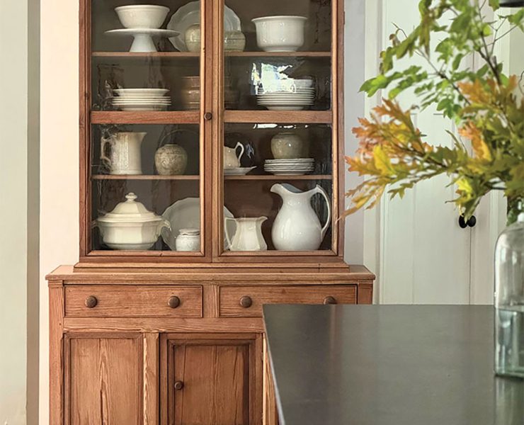 wooden hutch with white serveware and vase of fall leaves in dining room