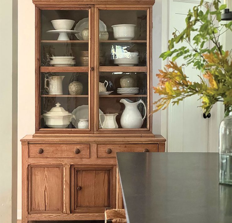 wooden hutch with white serveware and vase of fall leaves in dining room