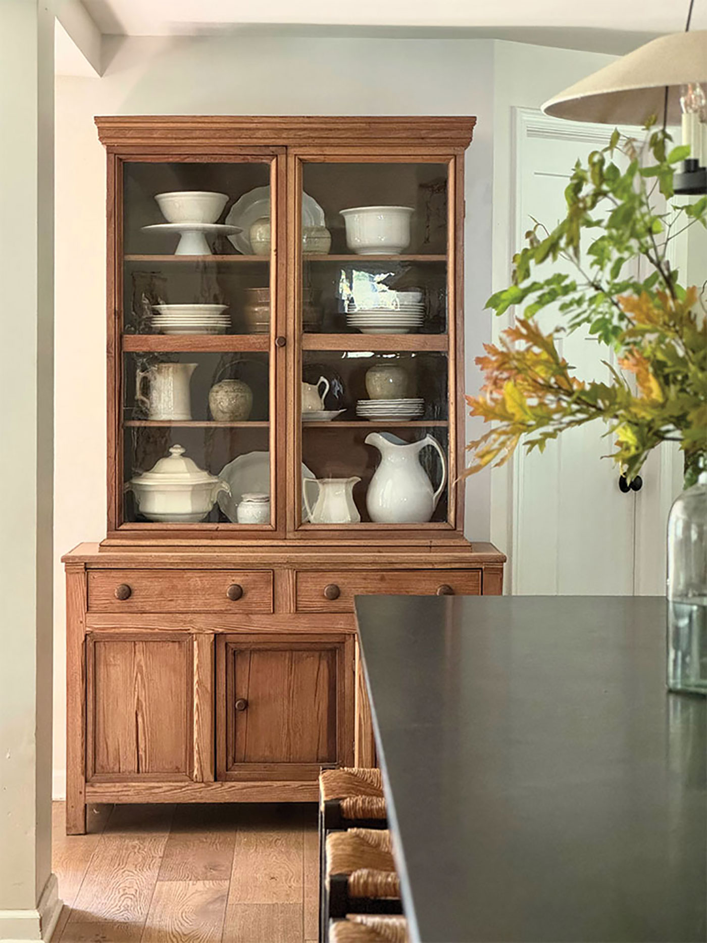 wooden hutch with white serveware and vase of fall leaves in dining room