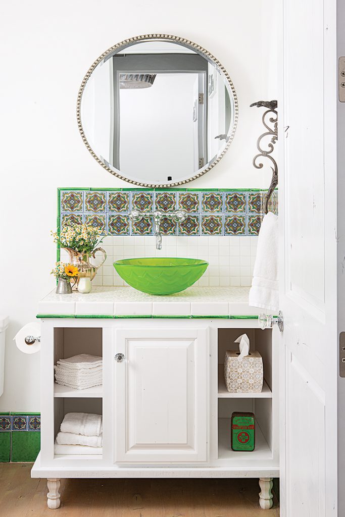 bathroom with fresh florals, green vessel sink and mosaic tile border