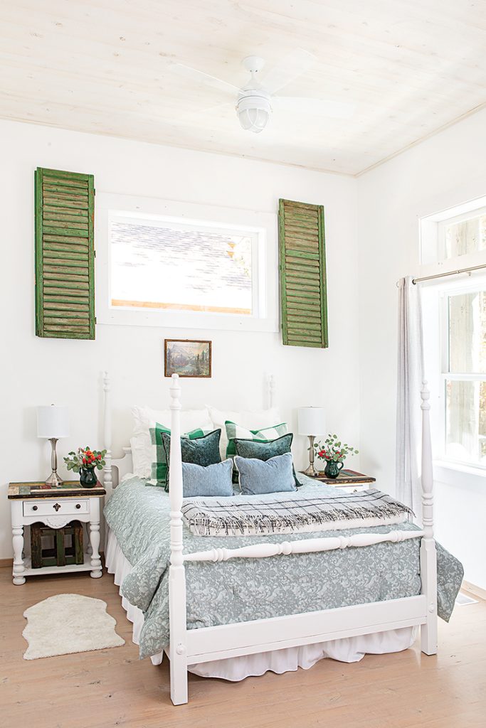 four poster bed with blue and green bedding, vintage shutters around window and fresh floral arrangements on nightstands