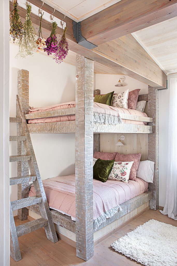 bunk beds with pink and green bedding, built in lighting sconces at the head and flowers drying in the rafters