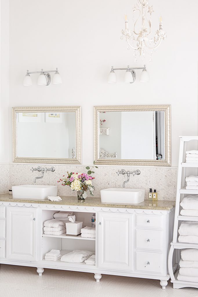 his and her sinks, white chandelier and white linens in Big Bear farmhouse cabin bathroom