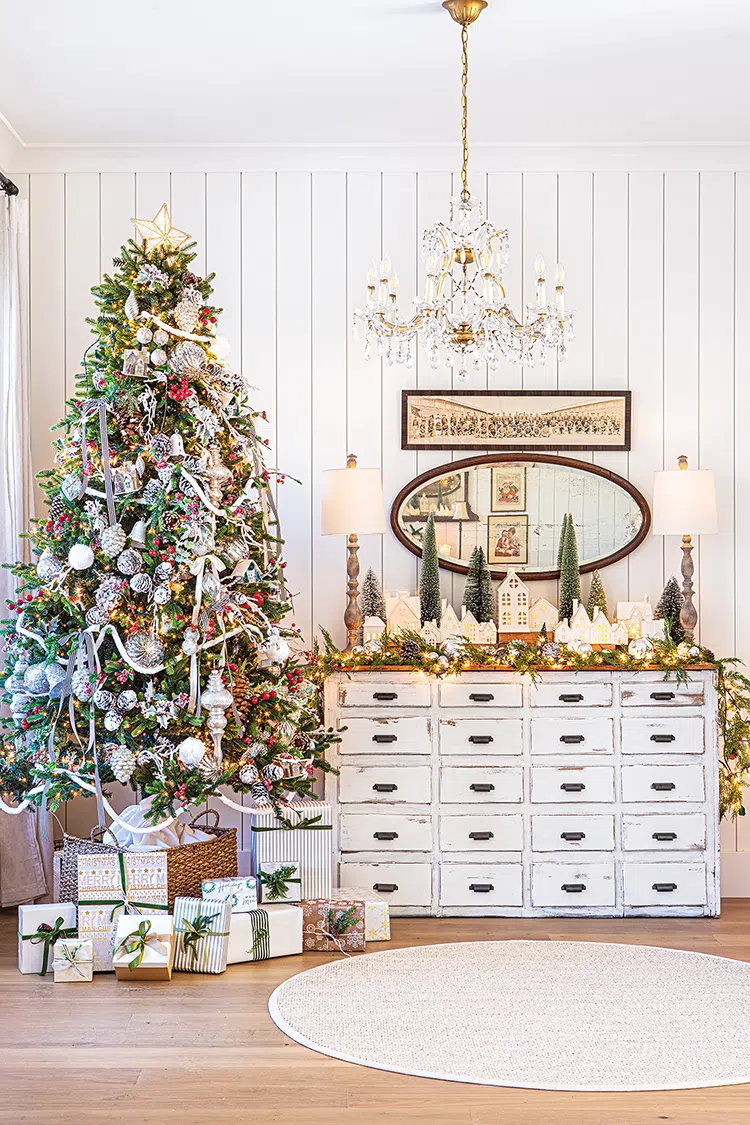 garland and Christmas village on top of vintage apothecary chest next to Christmas tree