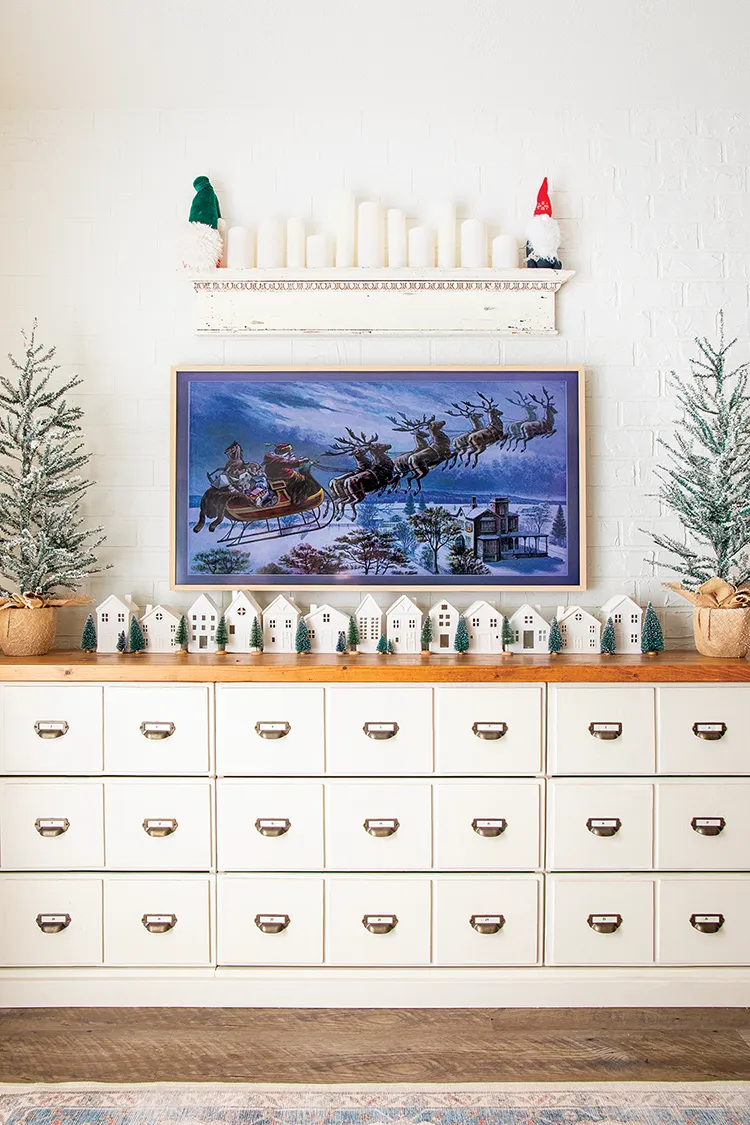 white vintage apothecary cabinet with white Christmas village and vintage Santa sleigh illustration