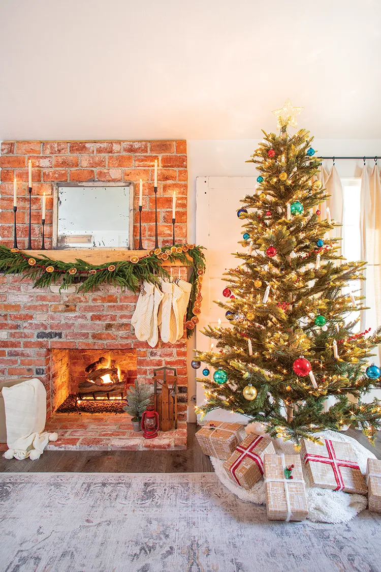 brick fireplace with white stockings and tapered candles next to Christmas tree in traditional red and green with gold and blue accents