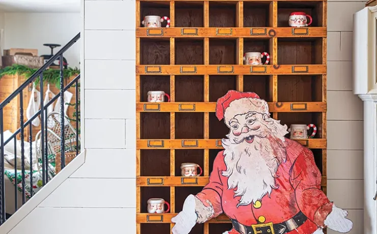 tall wooden shelf upcycled from hardware store with Santa cutout in front and Santa mugs inside