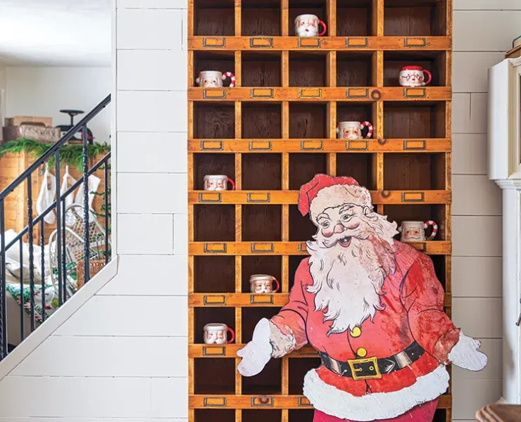 tall wooden shelf upcycled from hardware store with Santa cutout in front and Santa mugs inside