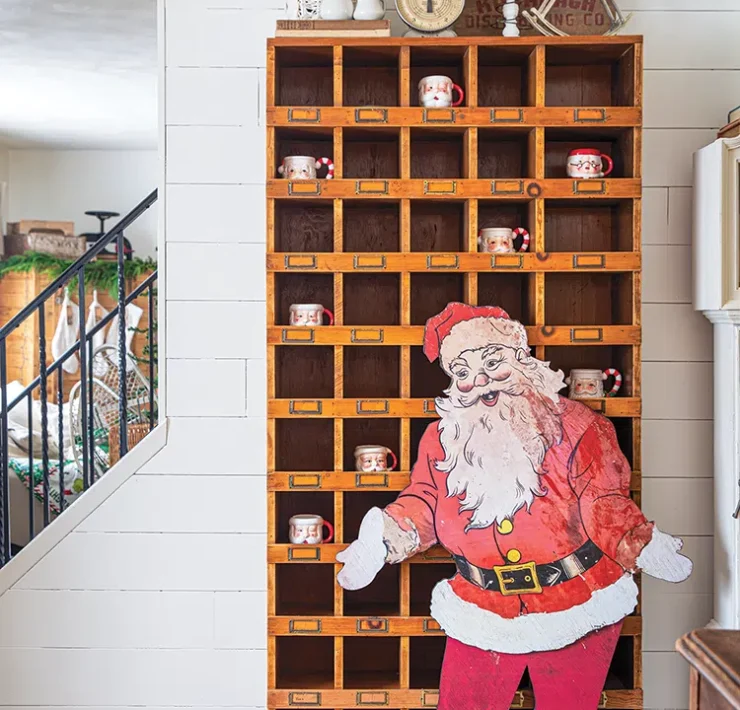 tall wooden shelf upcycled from hardware store with Santa cutout in front and Santa mugs inside