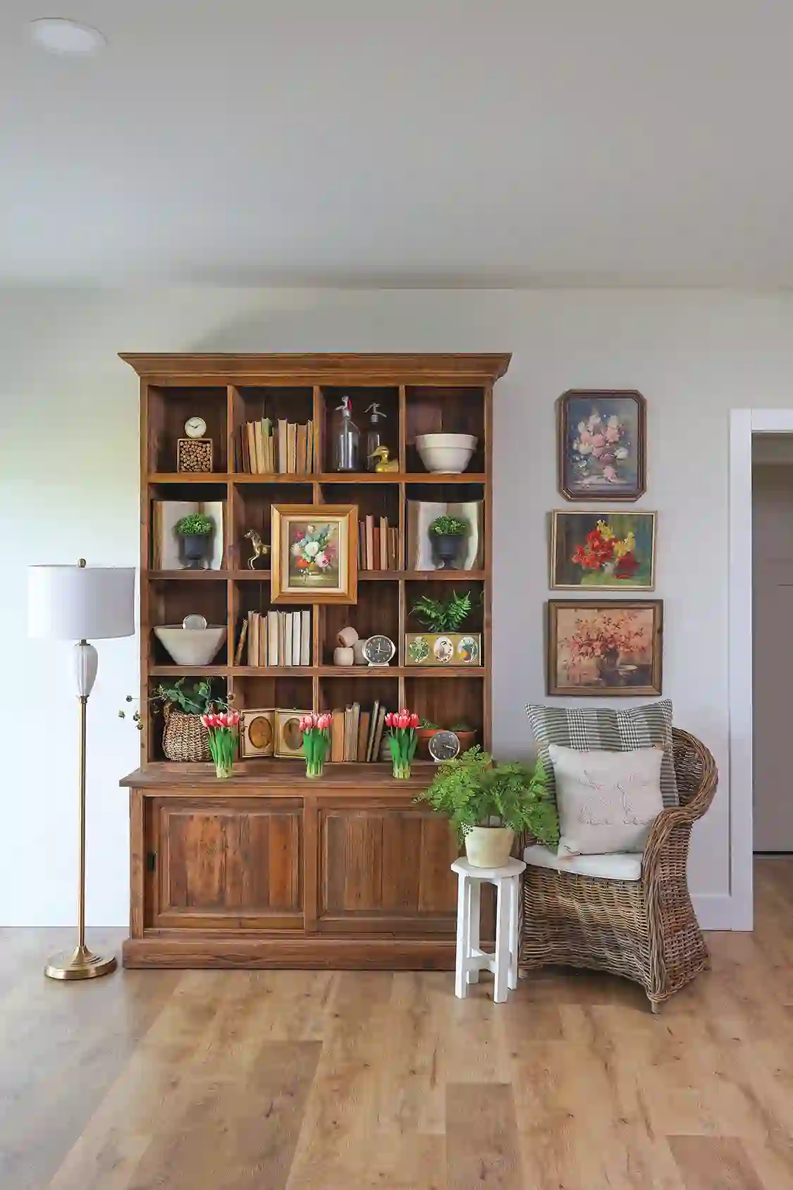 bookcase with plants, tulips and floral still life paintings beside it