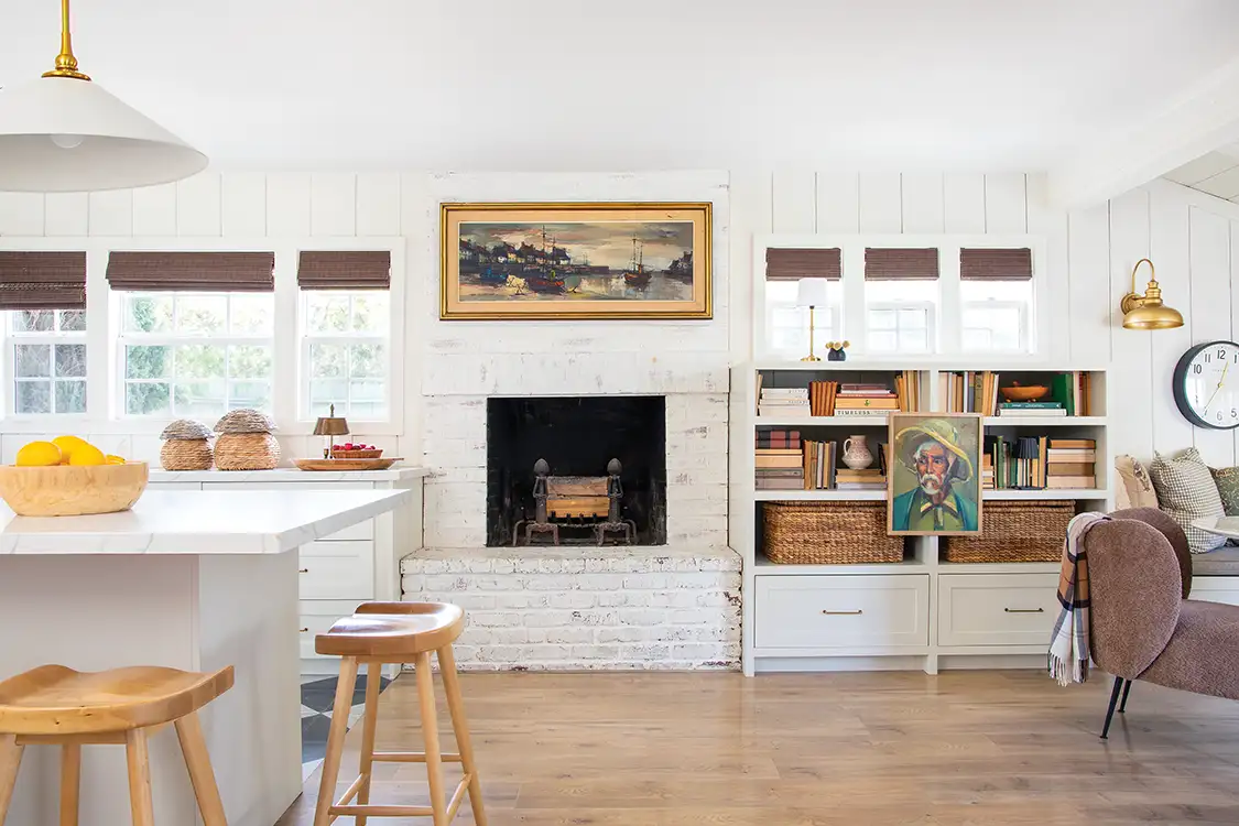 white painted brick fireplace and paintings as decor in white renovated kitchen and dining room