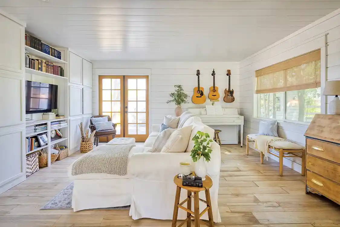 living room with wood floors white furniture and guitars hanging on shiplap walls