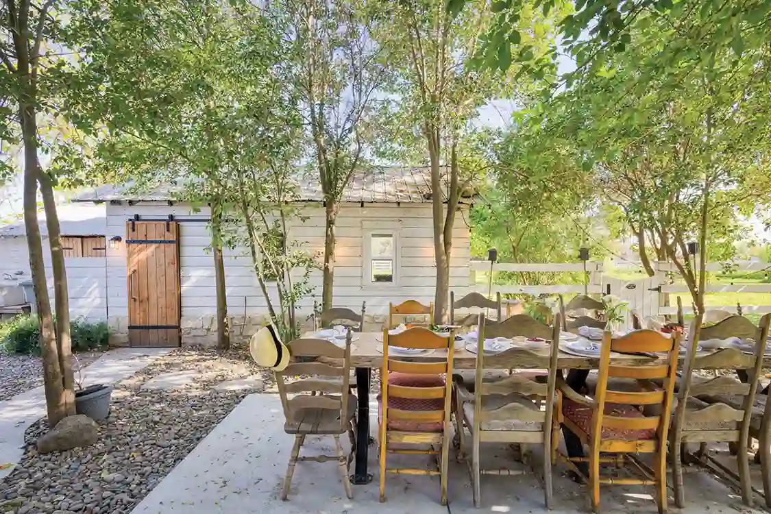 outdoor dining table with wooden chairs outside little house on large property